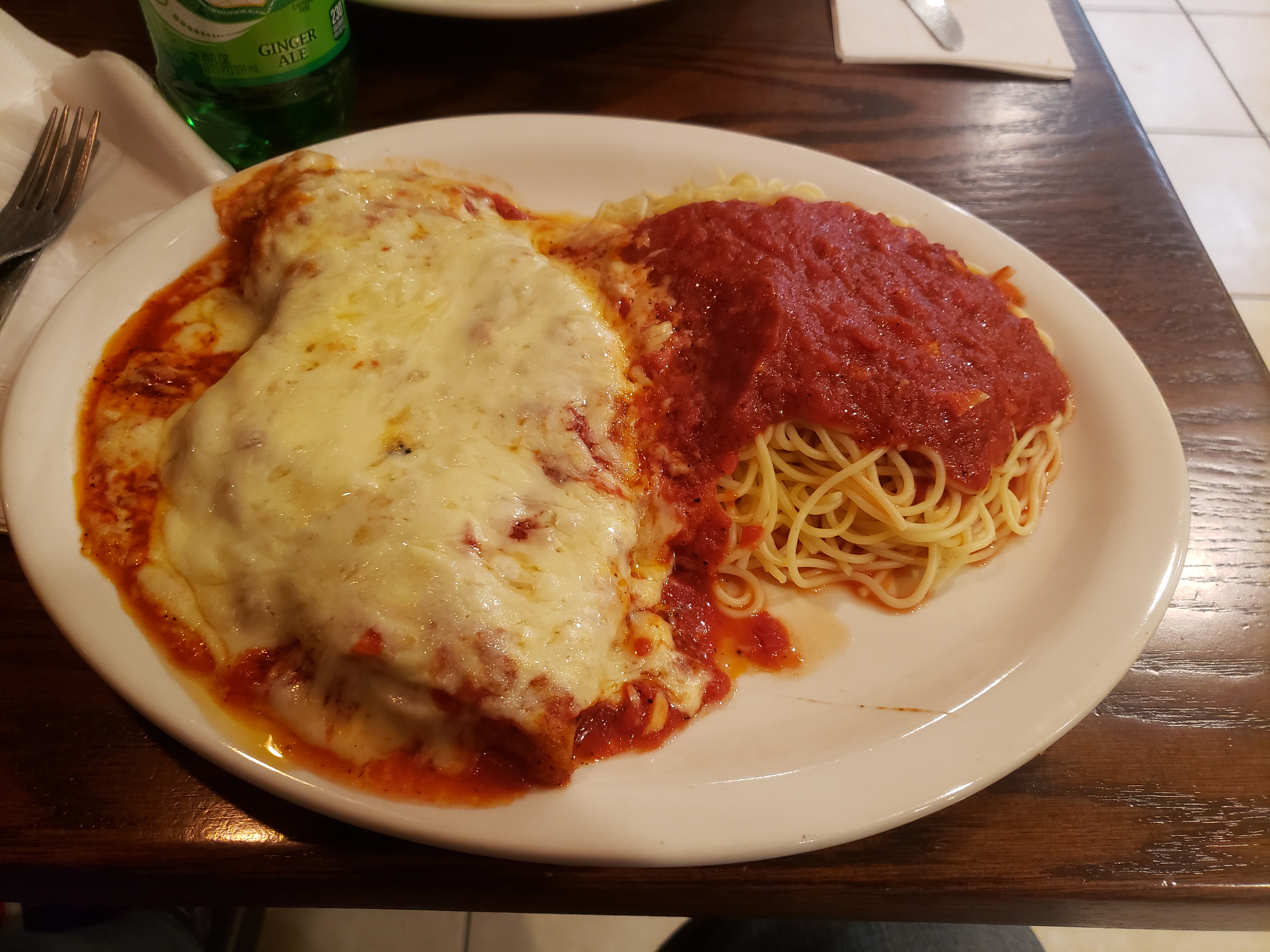 Plated eggplant parmesan with melted cheese and red sauce, served alongside spaghetti and a green beer bottle.
