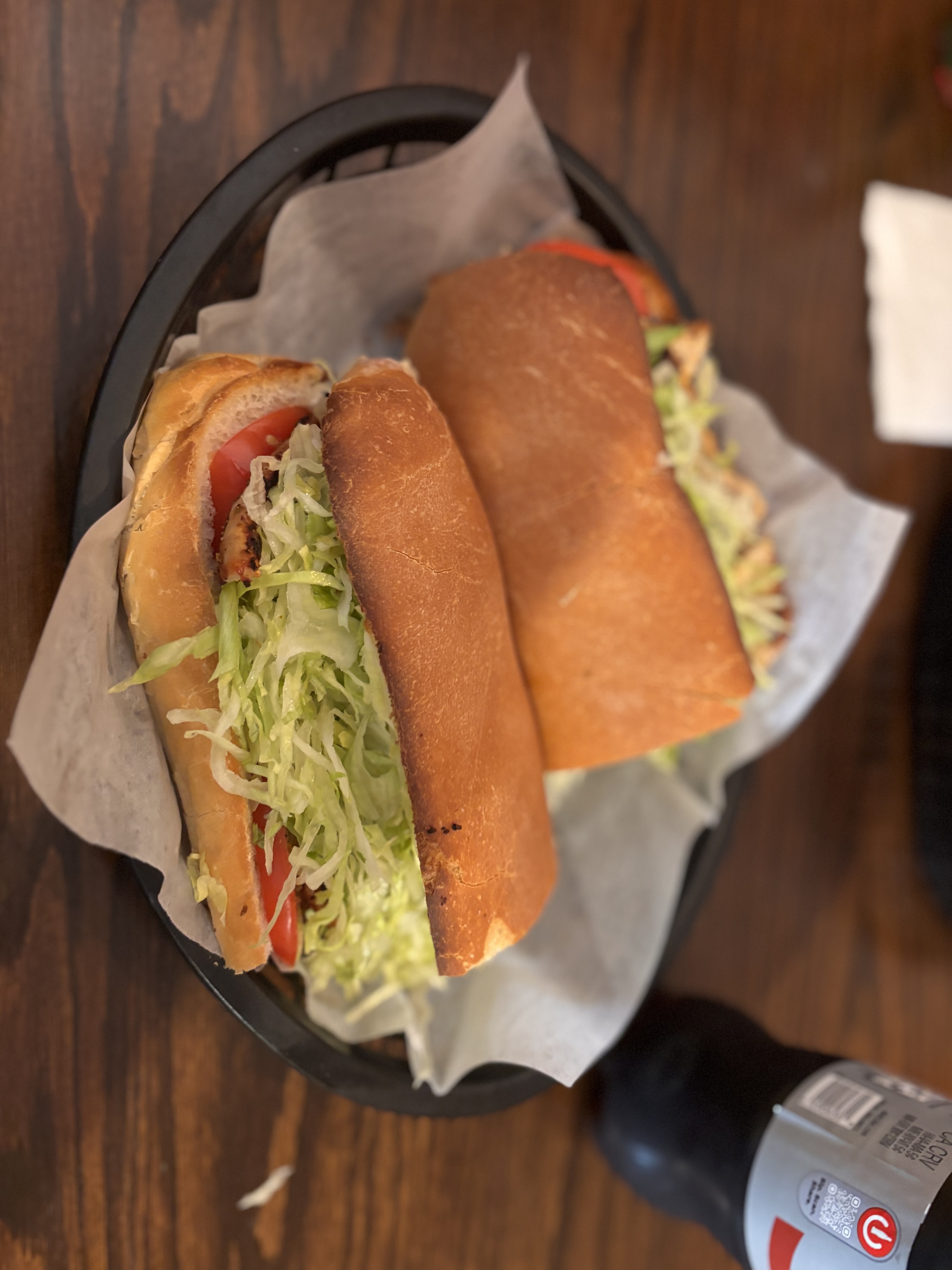 Two sandwiches on toasted rolls filled with shredded lettuce and tomato, wrapped in paper napkins.